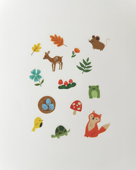 A collection of cute, whimsical forest-themed stickers arranged on a plain white background. The stickers include a brown deer, a green frog, a orange fox, a yellow bird, a green turtle, a brown mouse, a blue flower, an orange leaf, a red mushroom, and a brown nest with blue eggs.