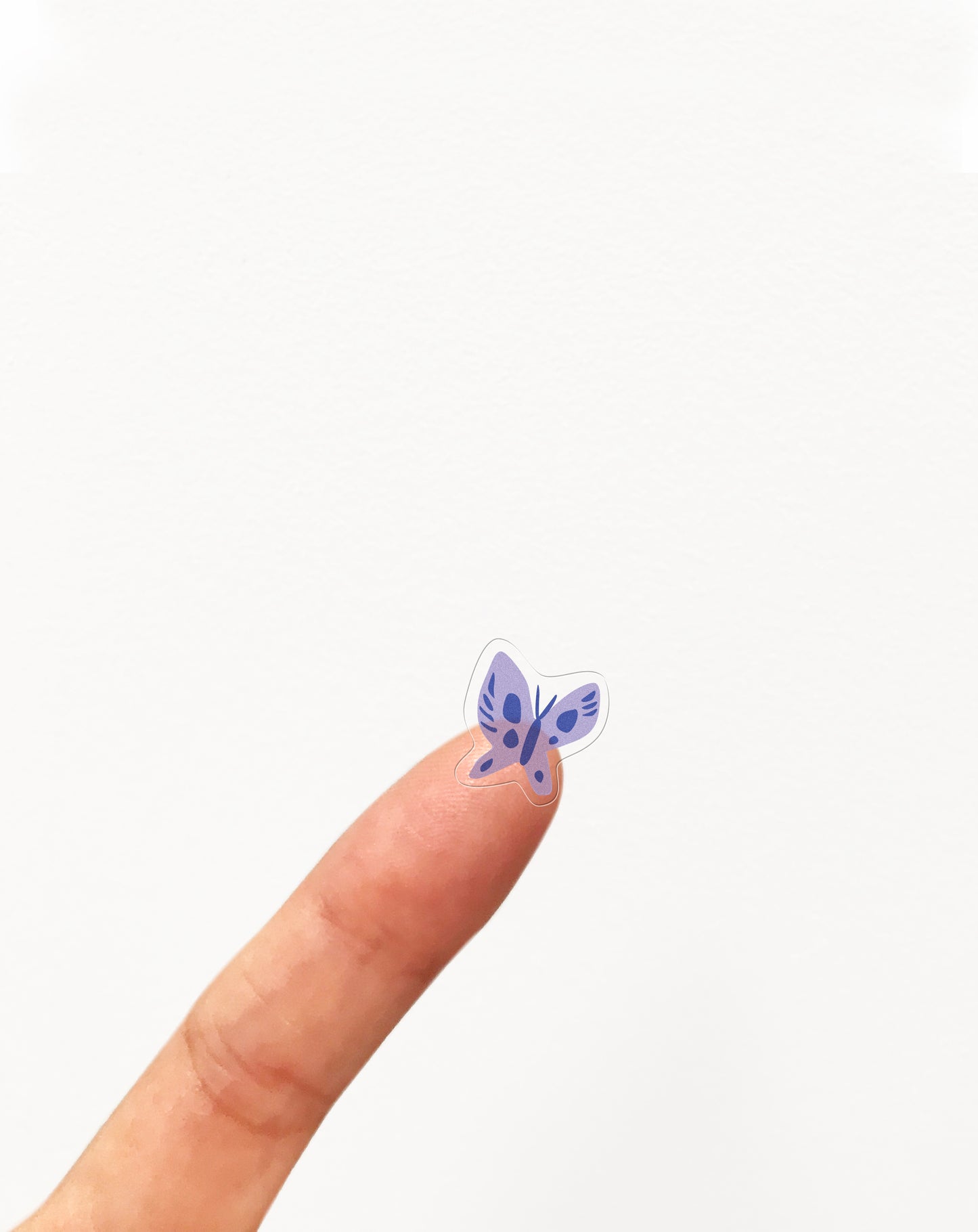A finger holding a small clear sticker of a butterfly.