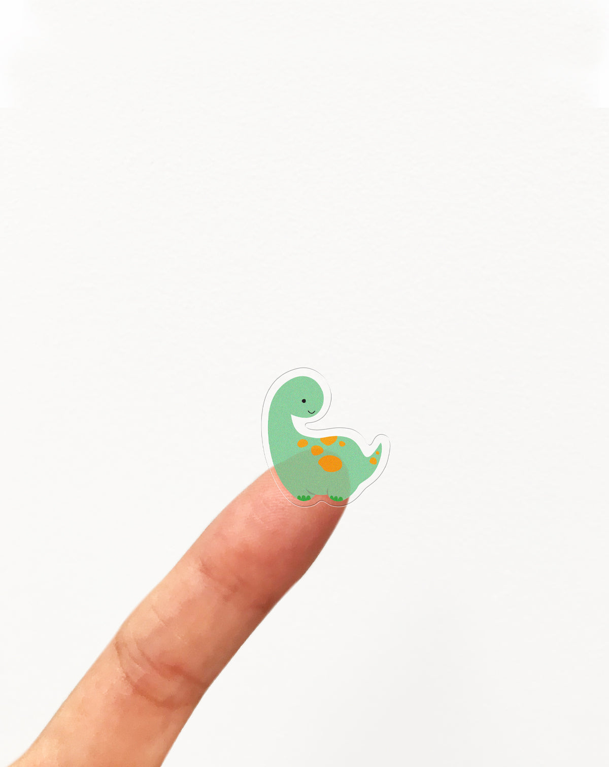 Small green dinosaur sticker on a finger against a white background