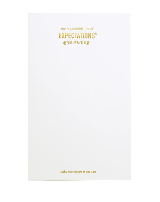 White notepad with gold foil text. "my reasonable list of EXPECTATIONS*" is printed at the top, and "*subject to change at any time" is printed at the bottom. 