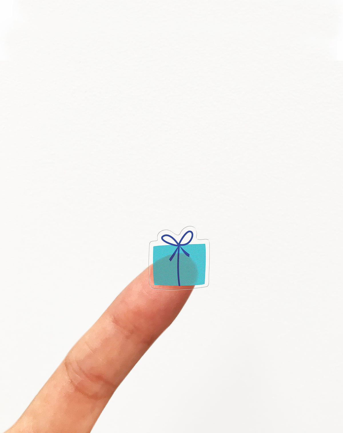 Sticker of small blue gift box with a bow on a finger against a white background