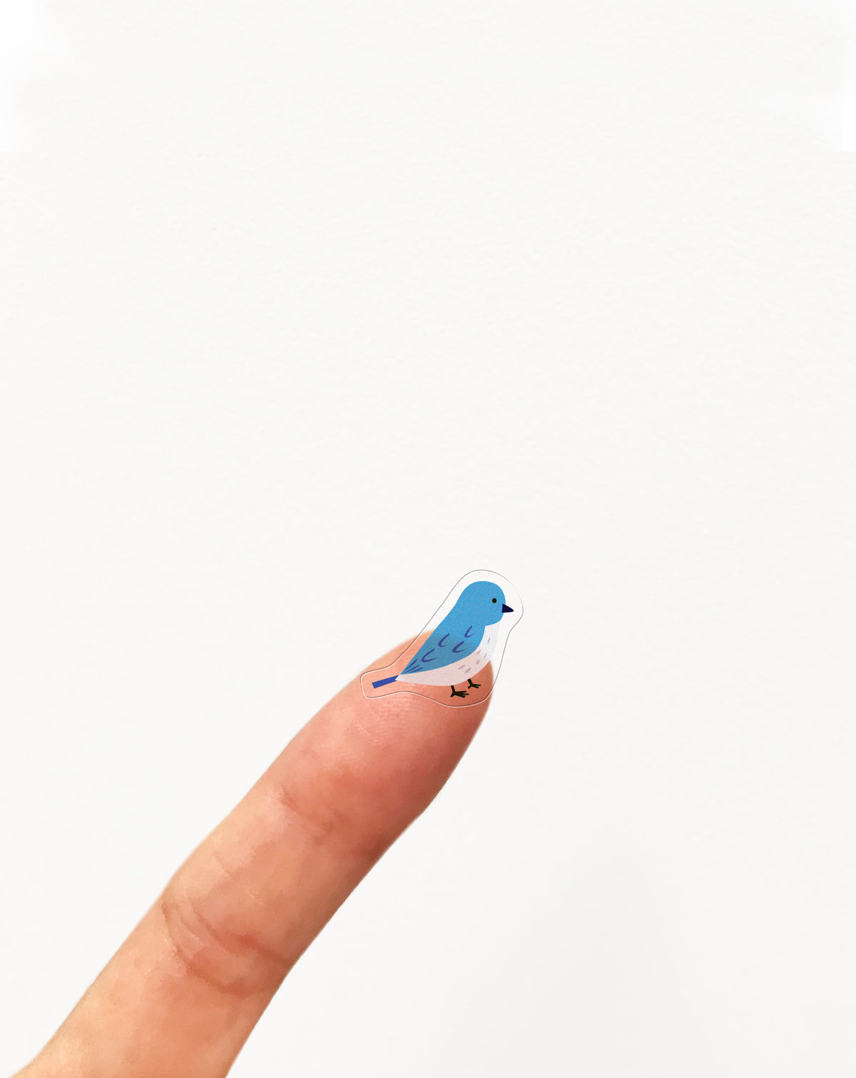 Small blue and white bird clear sticker on a finger against a white background