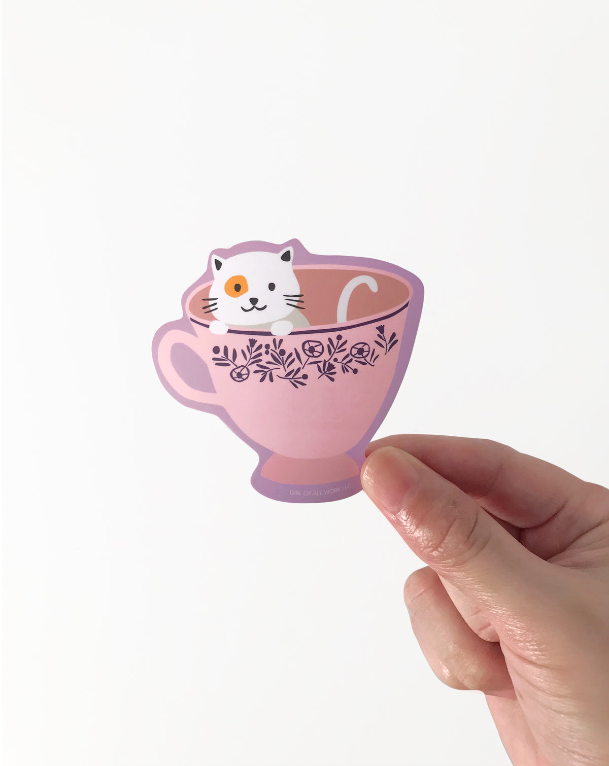 Vinyl Sticker of a pink teacup with cat design held by a hand on a white background