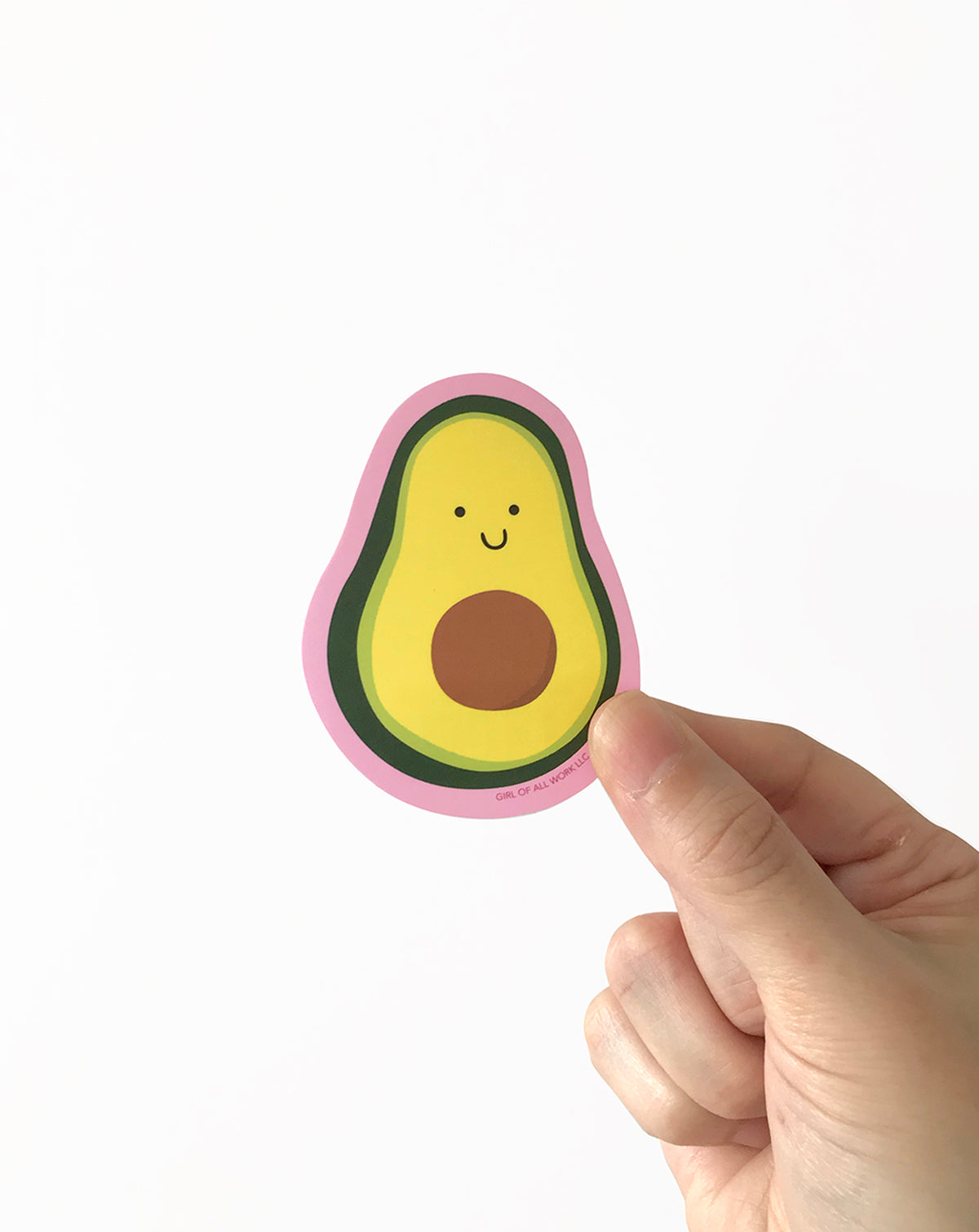 Hand holding a cute avocado-shaped vinyl sticker with a smiling face on a white background