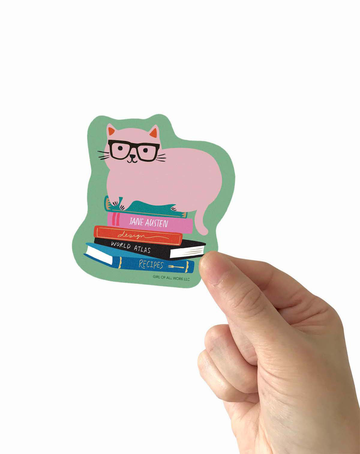 Hand holding a vinyl sticker of a cat with glasses and books on a white background
