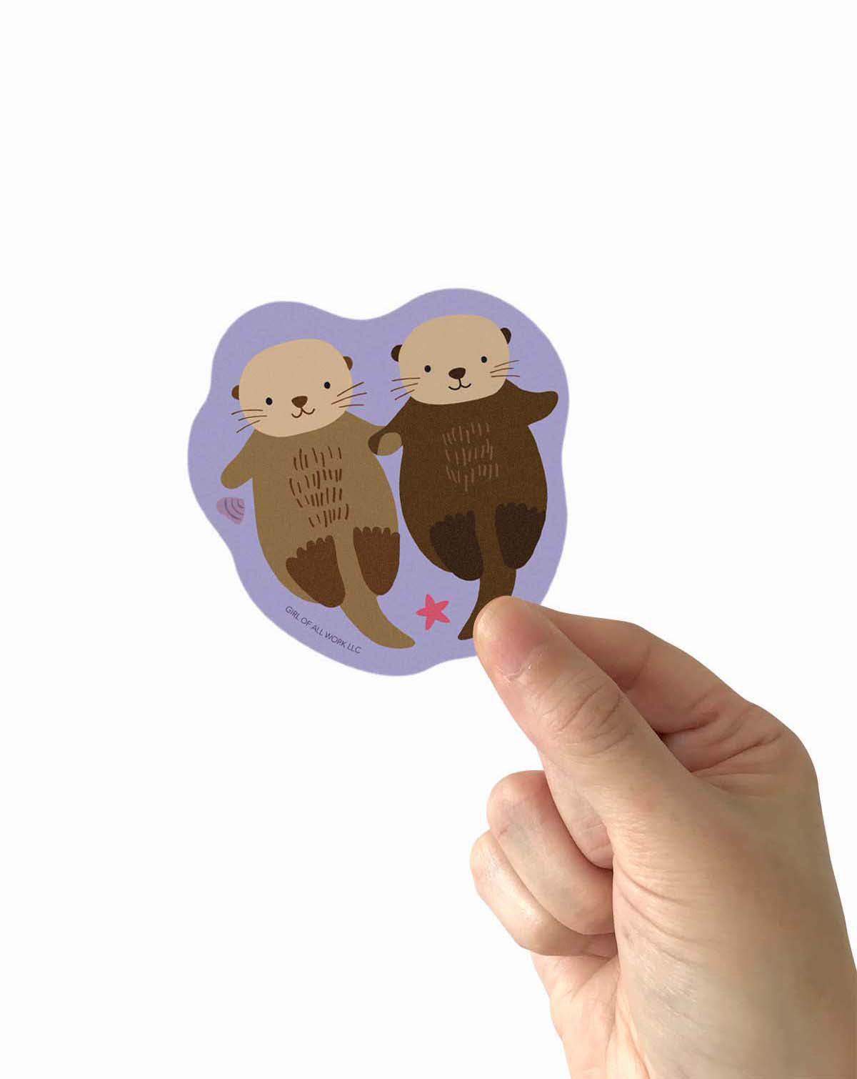 Hand holding a sticker with two otters and text on a white background