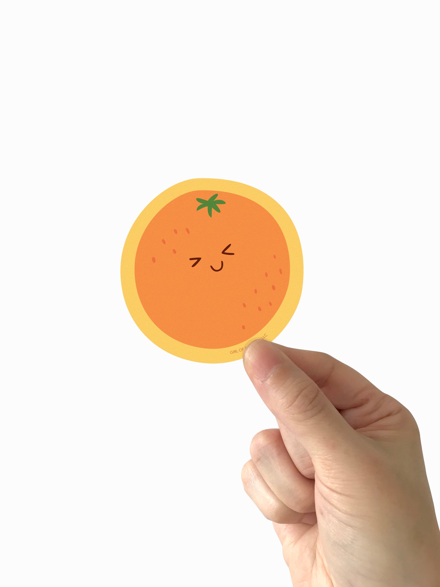 Hand holding a round, orange-colored vinyl sticker with a smiley face on a white background