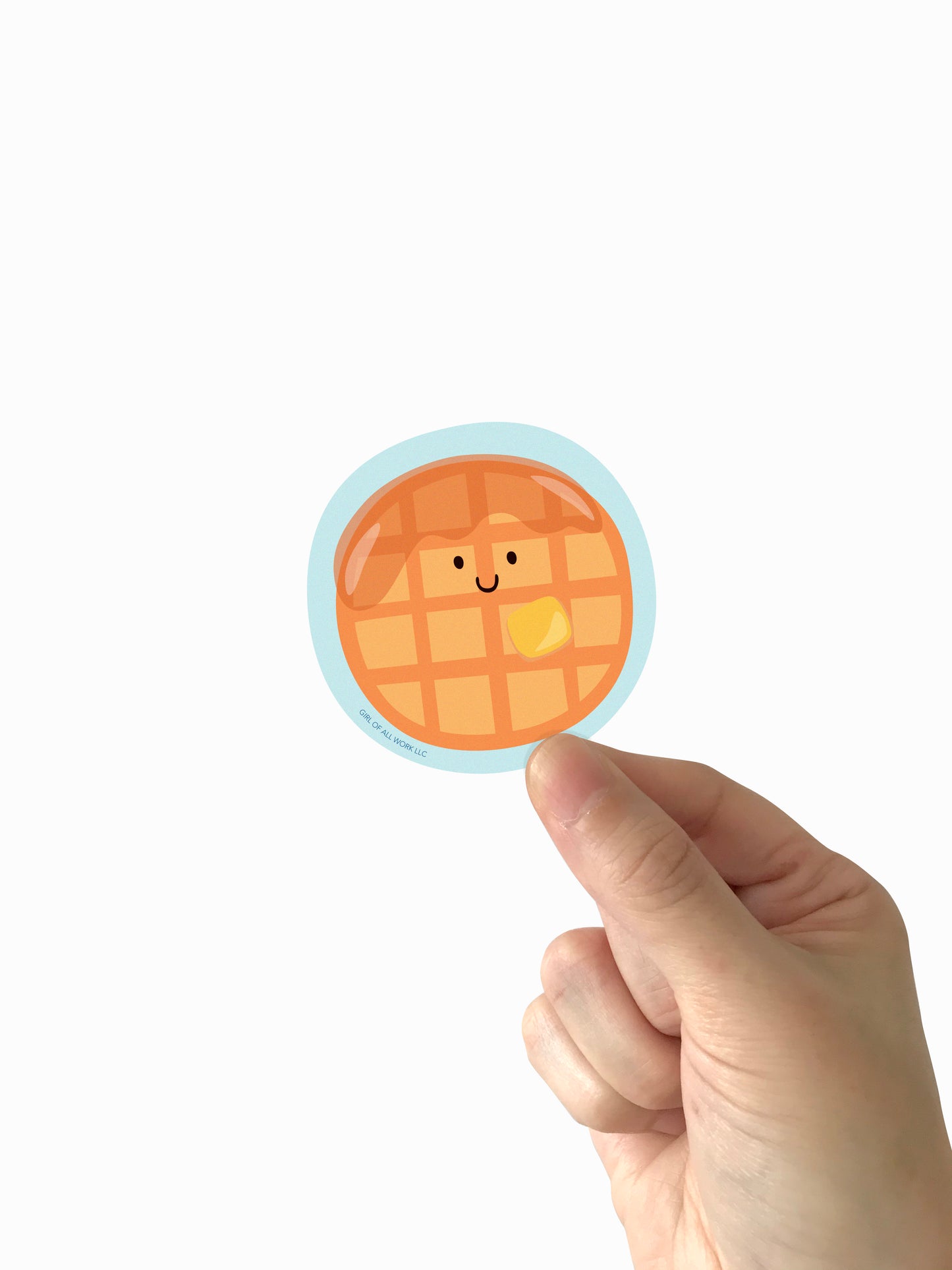 Hand holding a round sticker of a waffle with a smiling face on a white background
