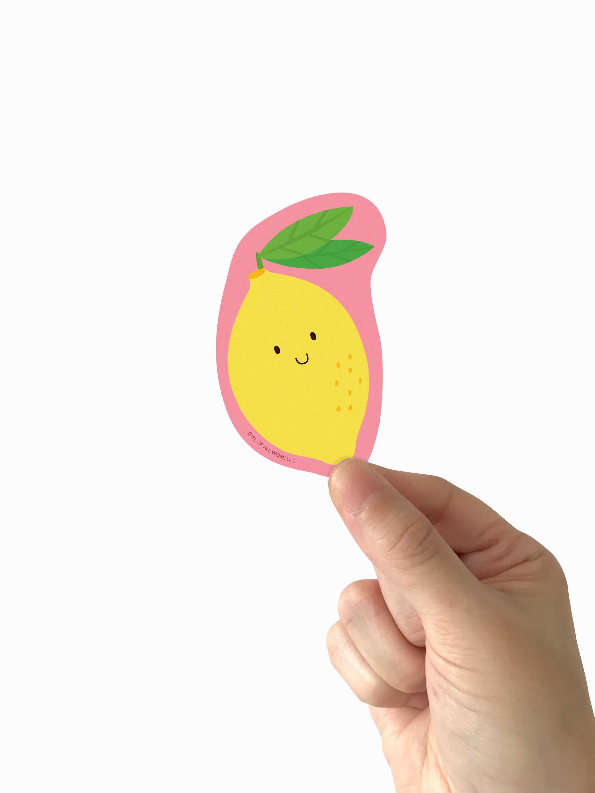 Hand holding a cute vinyl lemon-shaped sticker with a pink border on a white background