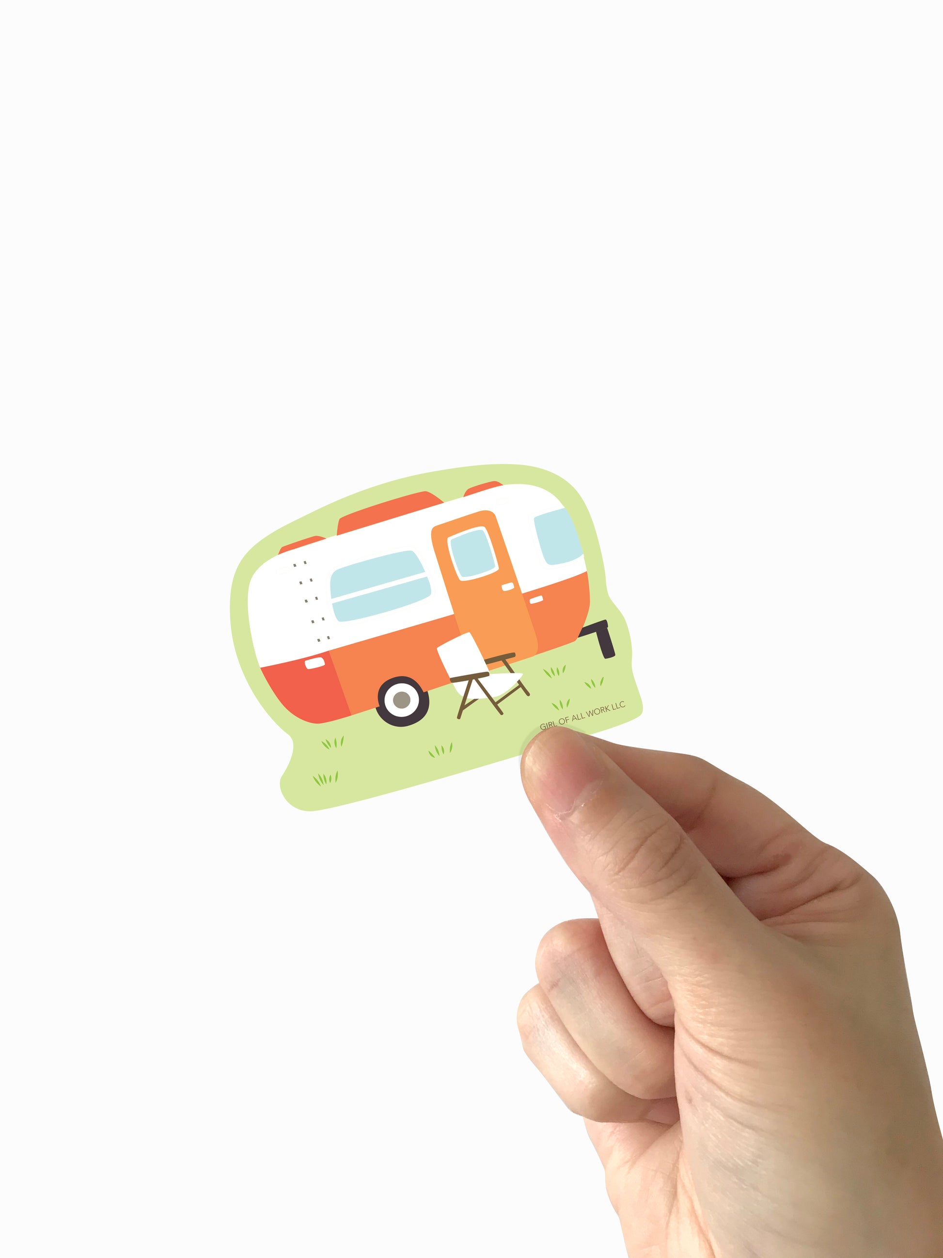 Hand holding a vinyl sticker with a camper illustration on a white background