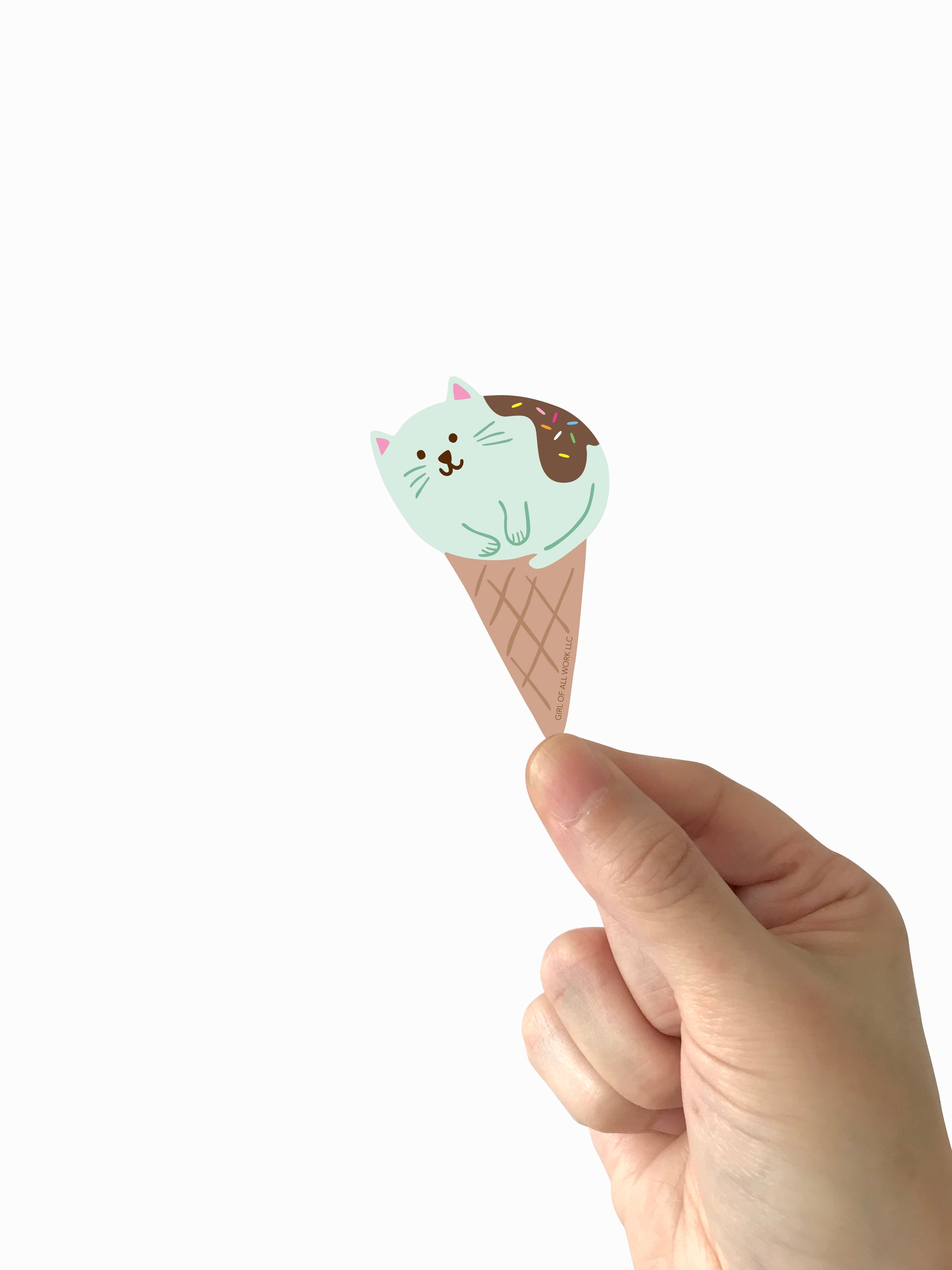 Hand holding a cute vinyl sticker featuring an ice cream cone with a cat on top against a white background
