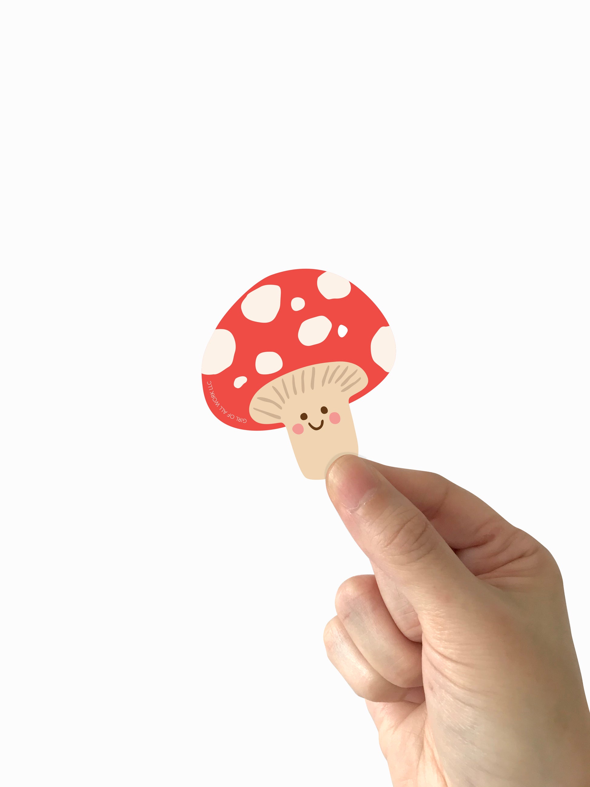 Hand holding a vinyl sticker mushroom with a red cap and white spots on a white background