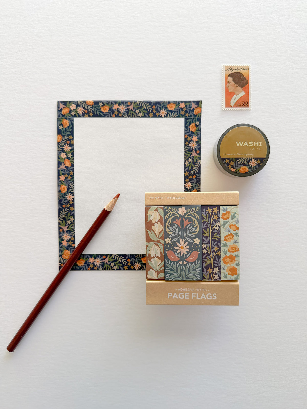 A white card decorated along the edge with floral tapestry washi tape, displayed alongside matching floral tapestry washi tape, a stamp, Floral Wallpaper Page Flags, and a brown colored pencil.