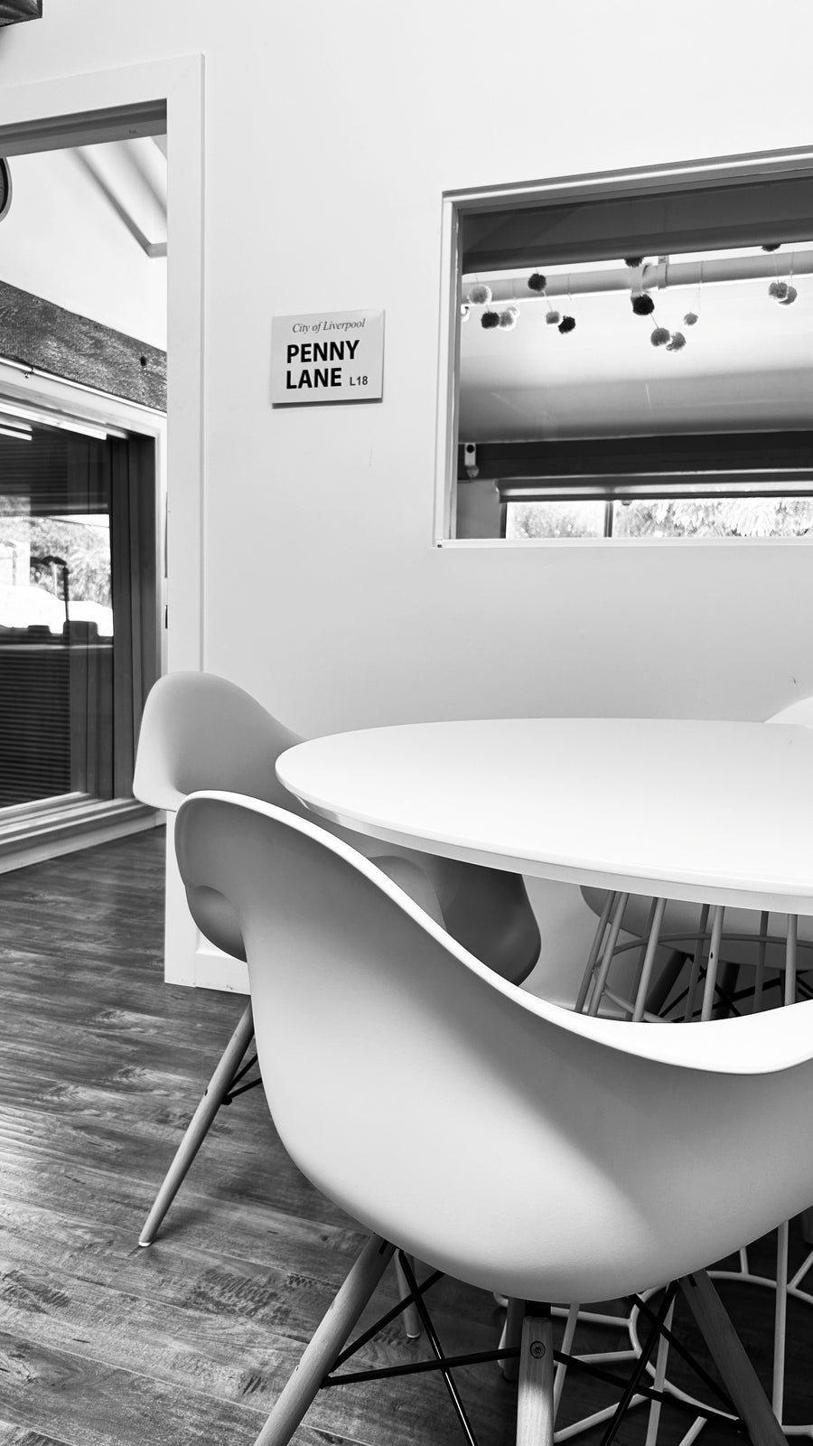 Modern conference area featuring a white oval table and three sculptural white chairs with metal legs, set in a minimalist interior with a wood floor and a sign reading 'PENNY LANE CO.' on the wall.
